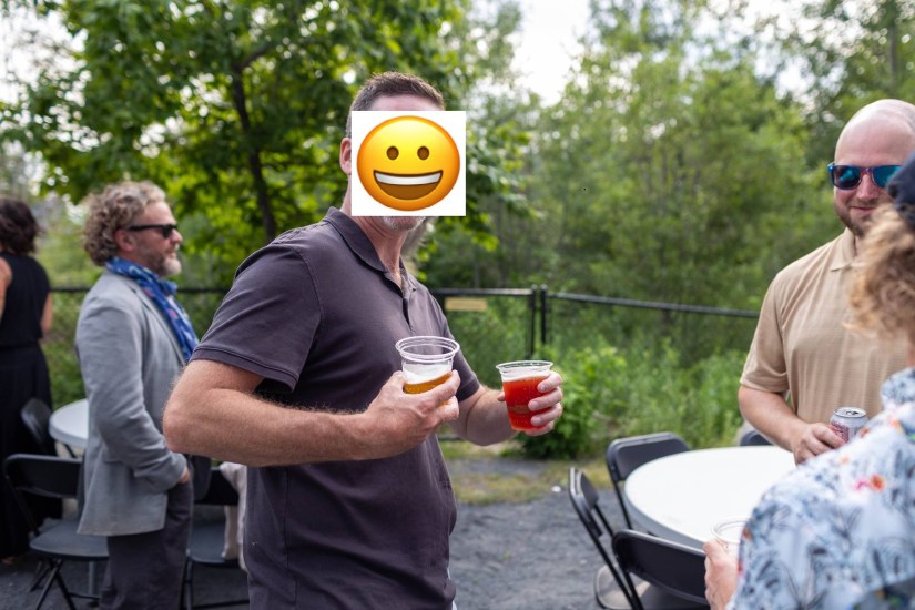 A group of people at an outdoor gathering, with one person holding two drinks, while others engage in conversation in the background.